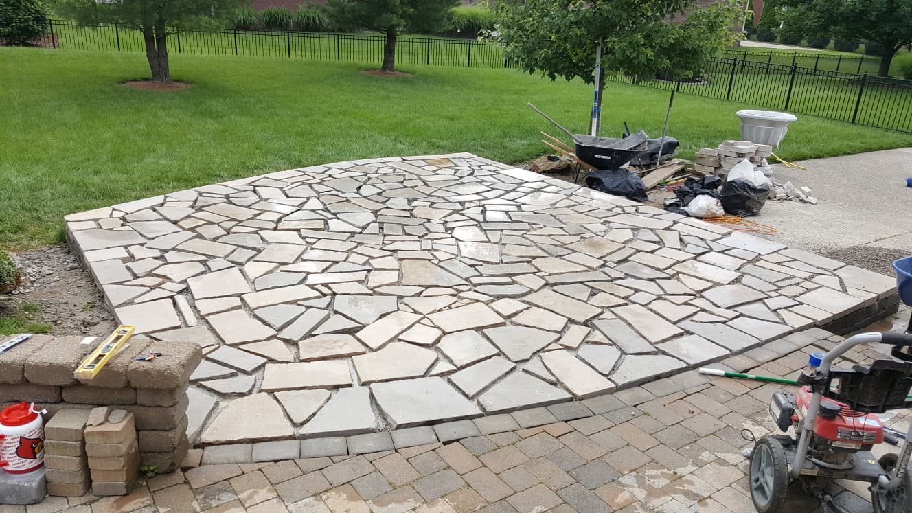 Flagstone patio bordered by brick pavers on a lawn.