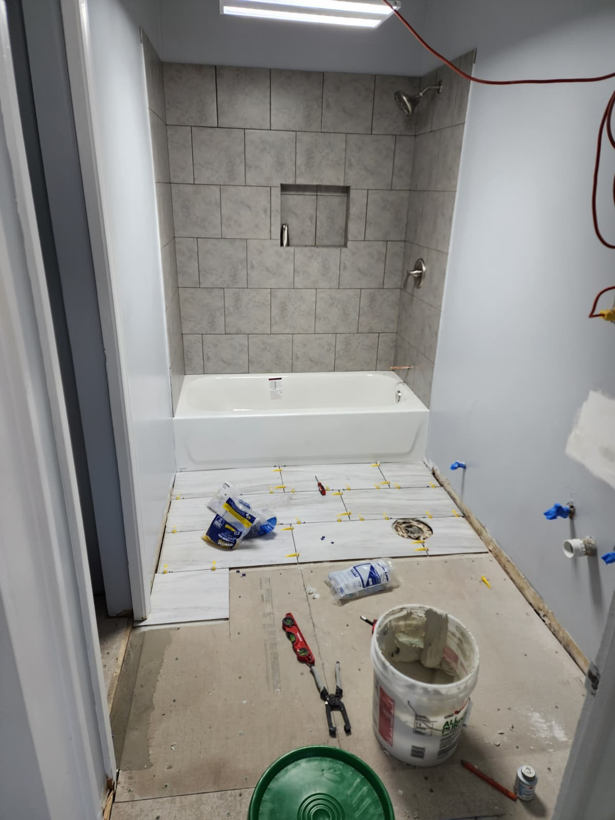 Bathtub surround tiled in gray with a niche and floor tile installation in progress.