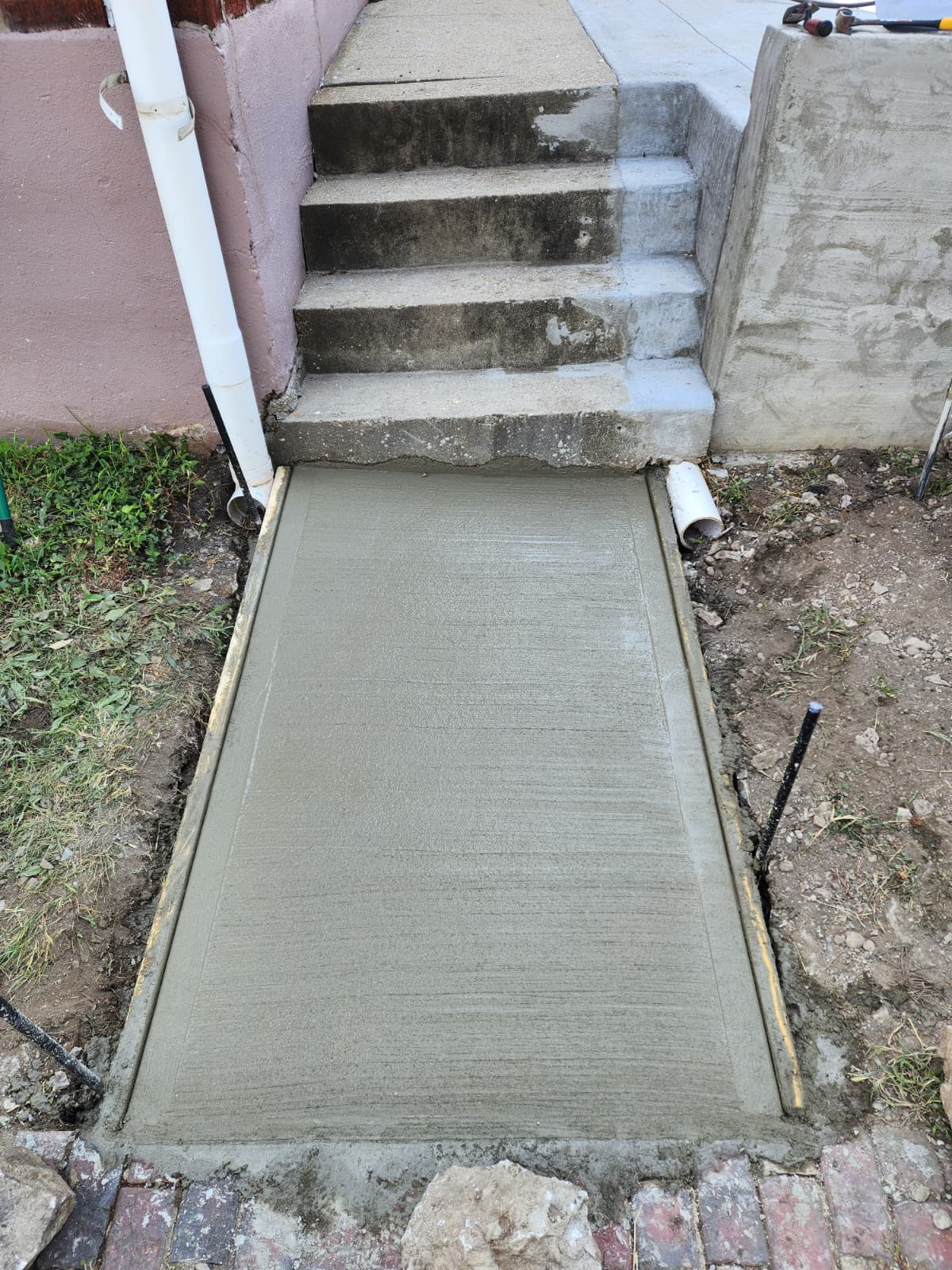 Fresh concrete ramp poured at the base of exterior steps.