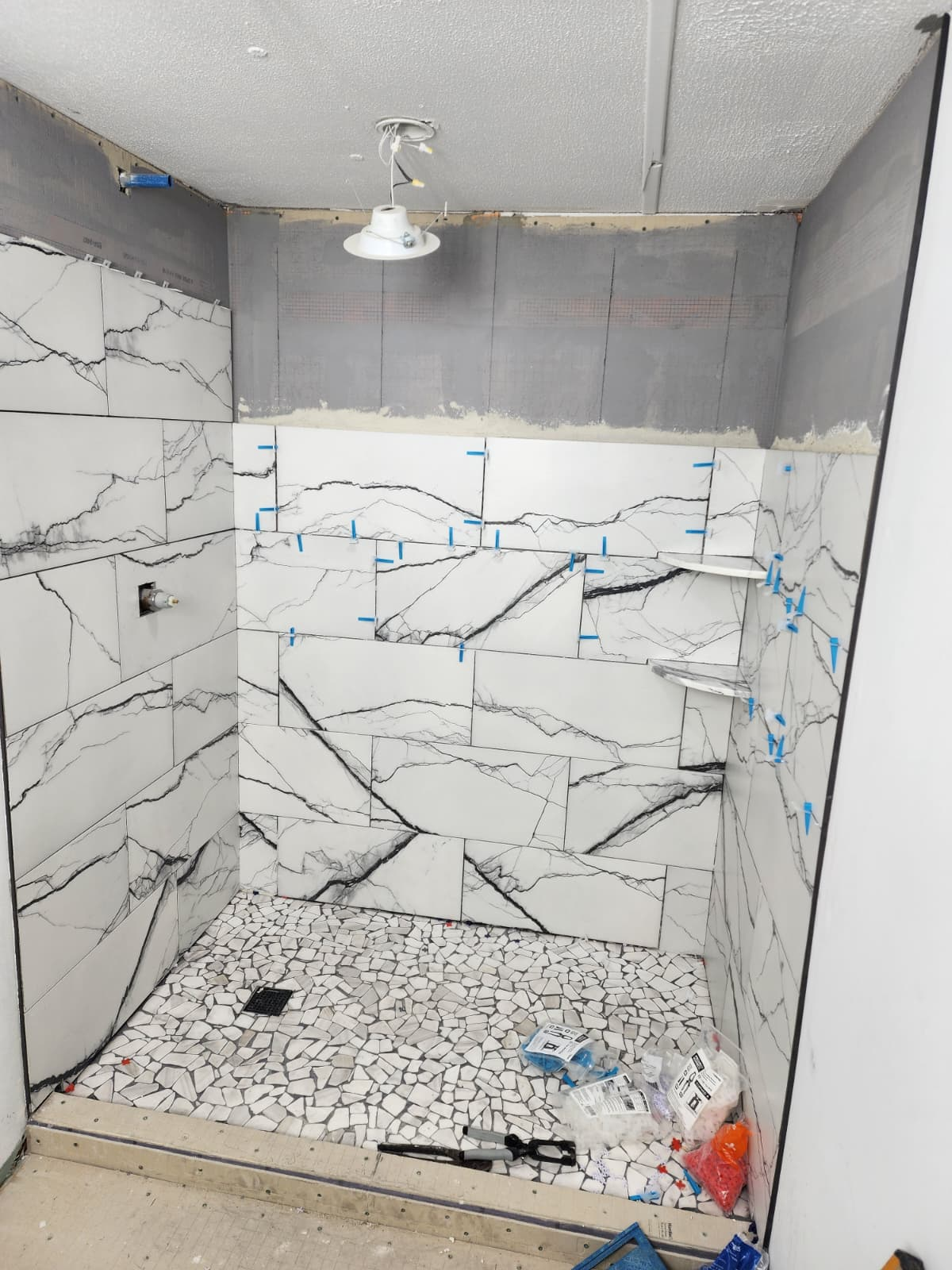 White marble-look tile installed on shower walls with leveling clips in place.